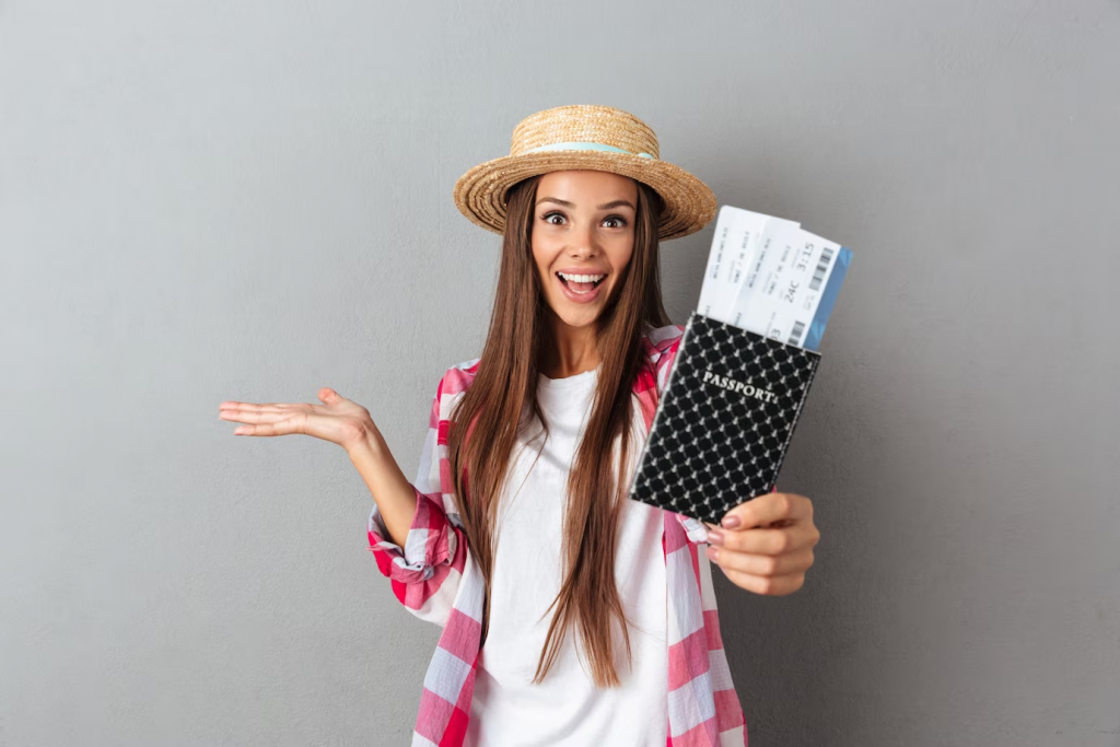 close up portrait of a smiling happy woman traveller in straw hat showing passport with plane tickets