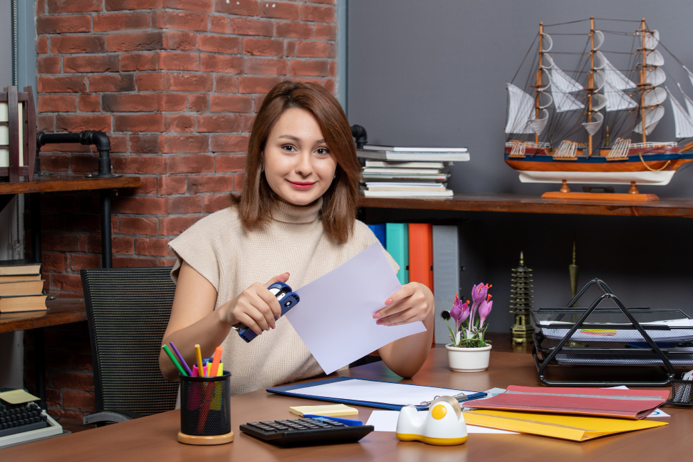 glad woman using stapler sitting at desk in office