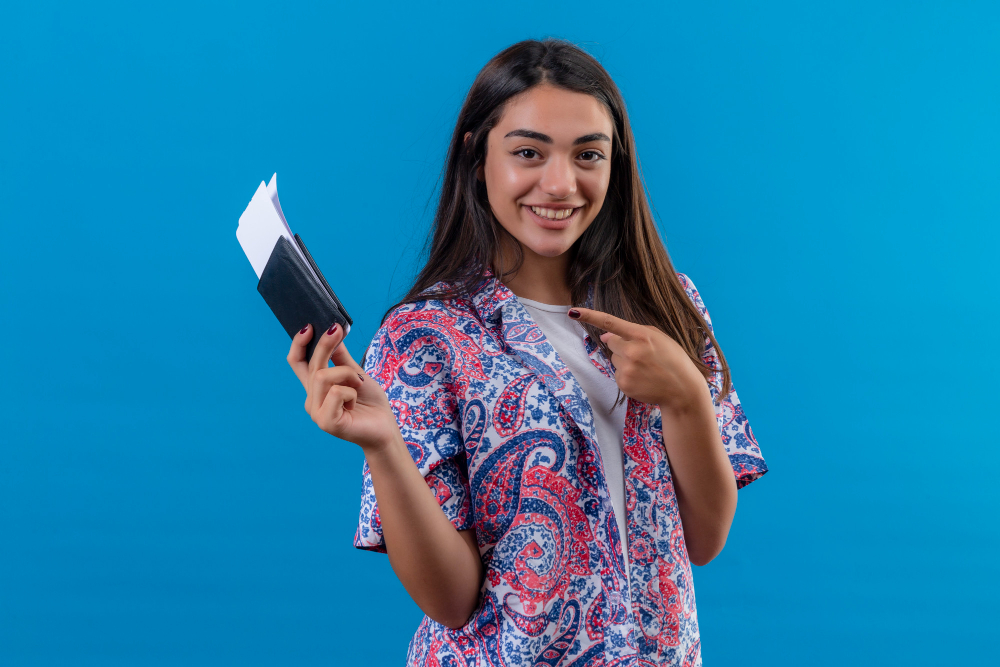 young beautiful woman tourist holding passport with tickets pointing with index finger to them smiling